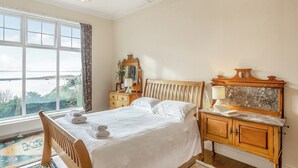 A bedroom with a large window, a wooden bed, a nightstand with a lamp, and a dresser. - 2 bedroom accommodation in Barmouth (Barmouth)