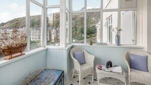 A cozy room with large windows, wicker chairs, a vintage ship model, and a blue trunk. - 2 bedroom accommodation in Barmouth (Barmouth)