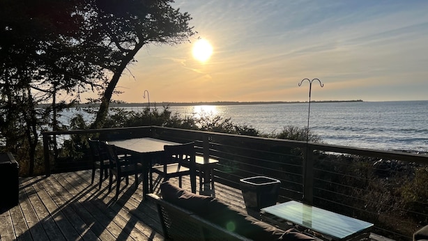 A wooden deck with outdoor furniture, overlooking a body of water and a distant island.