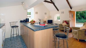 A modern kitchen with a bar area, wooden beams, and a view of the garden. - Lower Bushford Cottage (Hasguard, near Dale)