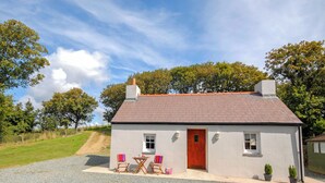 A small house with a red door, two windows, and a gravel driveway. - Lower Bushford Cottage (Hasguard, near Dale)