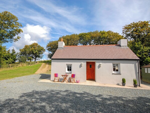 A small house with a red door, two windows, and a gravel driveway.