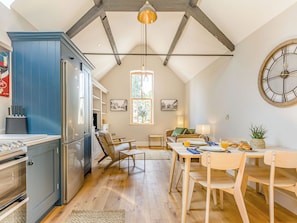 Une cuisine avec des meubles bleus, un coin repas avec une table et des chaises, et une grande horloge au mur.