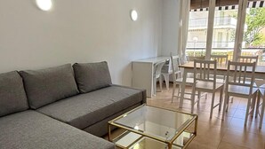 A modern living room with a grey sofa, a glass coffee table, and a dining area with white chairs and a table.