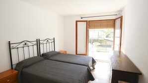 A bedroom with two beds, a wooden desk, and a balcony with a view.