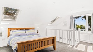 A bedroom with a wooden bed, a white railing, and a large window with a view of trees. - 2 bedroom accommodation in Pwlheli (Pwlheli)