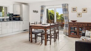 A modern kitchen with white cabinets, a dining table with chairs, and a view of the outdoors through a glass door. - 2 bedroom accommodation in Pwlheli (Pwlheli)