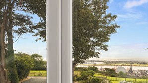 A view through a window of a residential area with a river, greenery, and a church spire. - 2 bedroom accommodation in Pwlheli (Pwlheli)