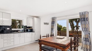 A modern kitchen with white cabinets, a wooden dining table, and a view of the outdoors. - 2 bedroom accommodation in Pwlheli (Pwlheli)