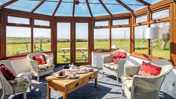 Ein Wintergarten mit Korbmöbeln, einem Holztisch und Blick ins Grüne.