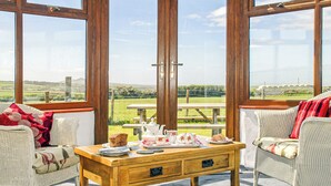 Ein Wintergarten mit Korbmöbeln, einem Holztisch mit Teeservice und Blick auf die Landschaft.