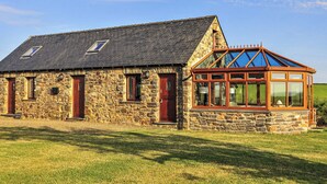 Ein Steinhaus mit geneigtem Dach, ein kleiner Anbau mit Glaskuppel und ein gepflegter Rasen.