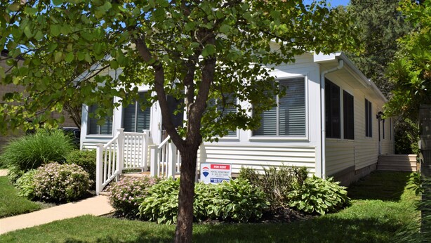 A single-story mobile home with a white exterior, a front porch, and a small garden area with various plants and shrubs. - Walk Everywhere! Pet Friendly Rehoboth Beach Home Sleeps 10 (Rehoboth Beach)