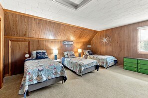 Une chambre avec trois lits, des murs en bois, une décoration sur le thème des étoiles et une commode verte.