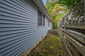 Un étroit sentier mène à une maison bordée d’une clôture en bois d’un côté et d’un portail en métal de l’autre.