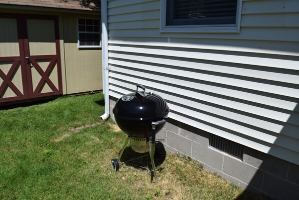 Ein Grill steht auf einer Rasenfläche neben einem Haus mit Garage und Fenster.
