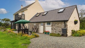 A two-story house with a sloped roof, a visible chimney, and a small porch with a green umbrella. - 3 bedroom accommodation in Druidstone Cross - near Nolton Haven (Haverfordwest)