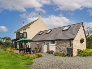 Une maison à deux étages, avec un toit en pente, une cheminée bien visible et un petit porche surmonté d’un parasol vert.