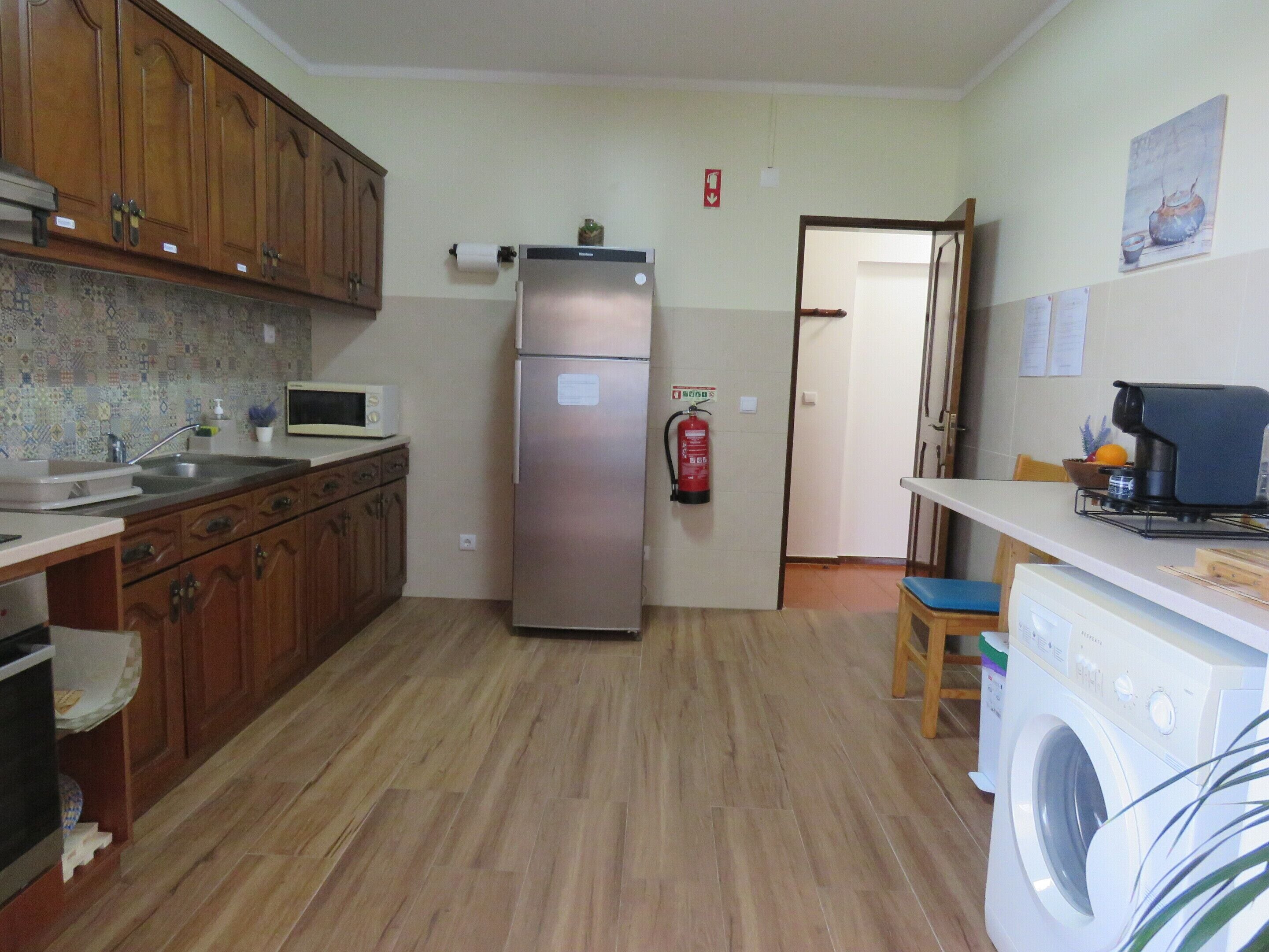 A kitchen with wooden cabinets, a stainless steel refrigerator, a microwave, a washing machine, and a fire extinguisher.