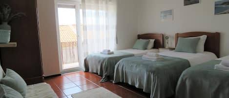 A hotel room with two beds, a sofa, a small table, and a view of the outdoors through a sliding door.