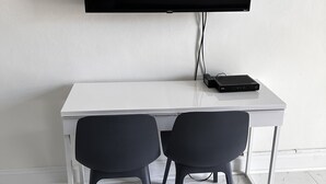 Una scrivania bianca con due sedie nere, un televisore a schermo piatto montato al muro e un dispositivo elettronico nero sulla scrivania.