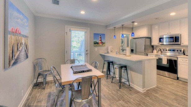 Une cuisine moderne avec des meubles blancs, des appareils en acier inoxydable et un îlot central doté de tabourets de bar.