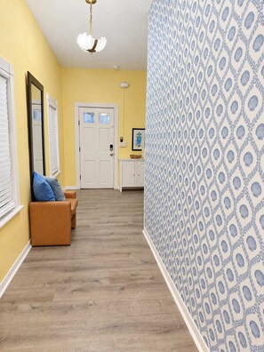 A hallway with a patterned wall, a door, a bench with cushions, and a ceiling light fixture.