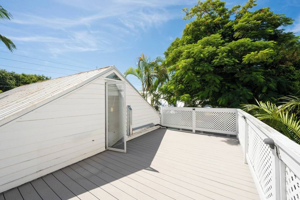 A wooden deck with a white railing, a clear sky, and lush green trees in the background.