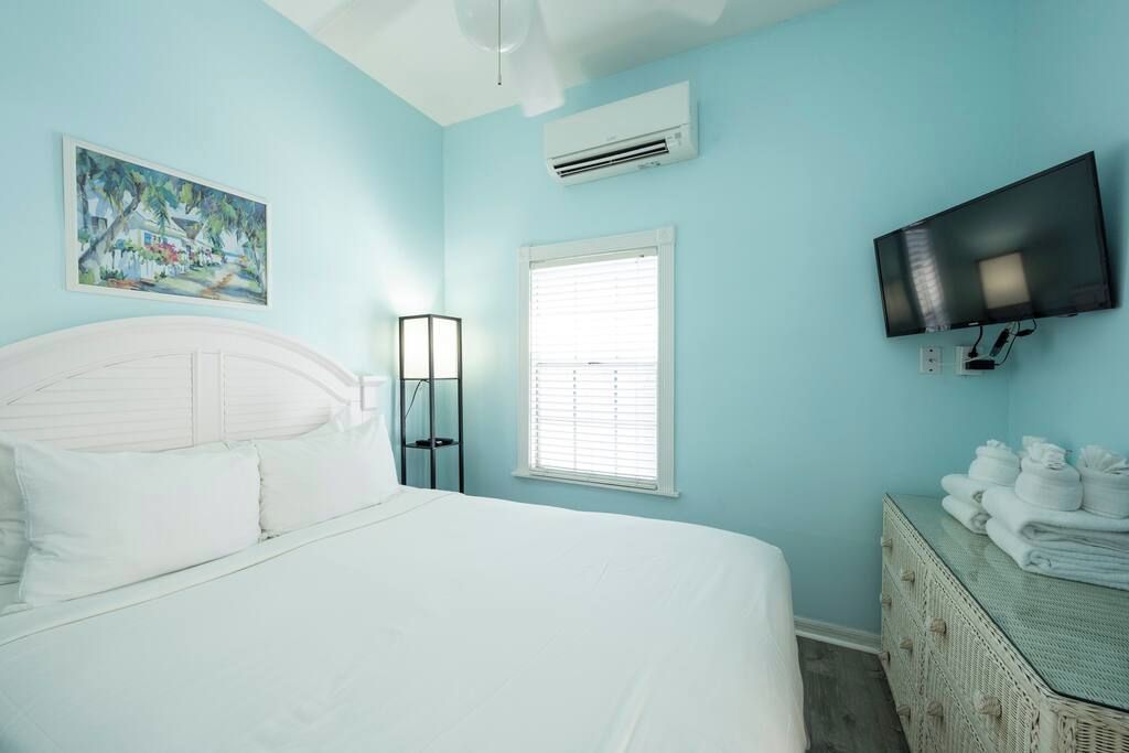 A bedroom with a bed, a television, a painting, and a window.