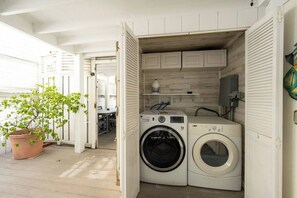 A compact laundry room with a washing machine and dryer, wooden cabinets, and a potted plant. - Hemingway's Neighbor: Hot Tub, Sundeck, Old Town (Key West)