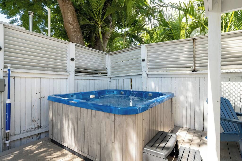 Un bain à remous en bois avec un bord bleu, entouré d’une clôture blanche, et une chaise bleue sur la droite.