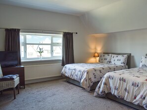 Une chambre d’hôtel avec deux lits, une télévision, une chaise, une fenêtre avec des rideaux et un radiateur.