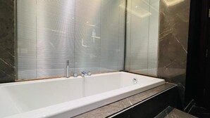 A modern bathroom with a large bathtub, frosted glass shower enclosure, and marble flooring. - The Prime Delhi (New Delhi)