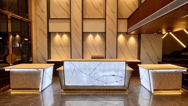 A modern lobby with marble walls, recessed lighting, and a central seating area with a marble table. - The Prime Delhi (New Delhi)