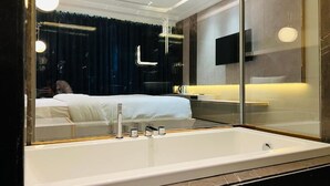 A modern bathroom with a large bathtub, a mirror, and a dark curtain backdrop. - The Prime Delhi (New Delhi)