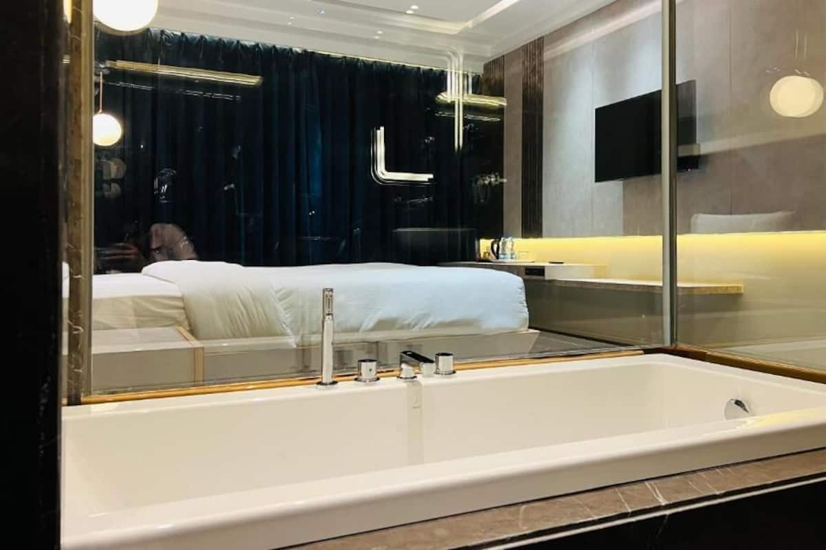 A modern bathroom with a large bathtub, a mirror, and a dark curtain backdrop.