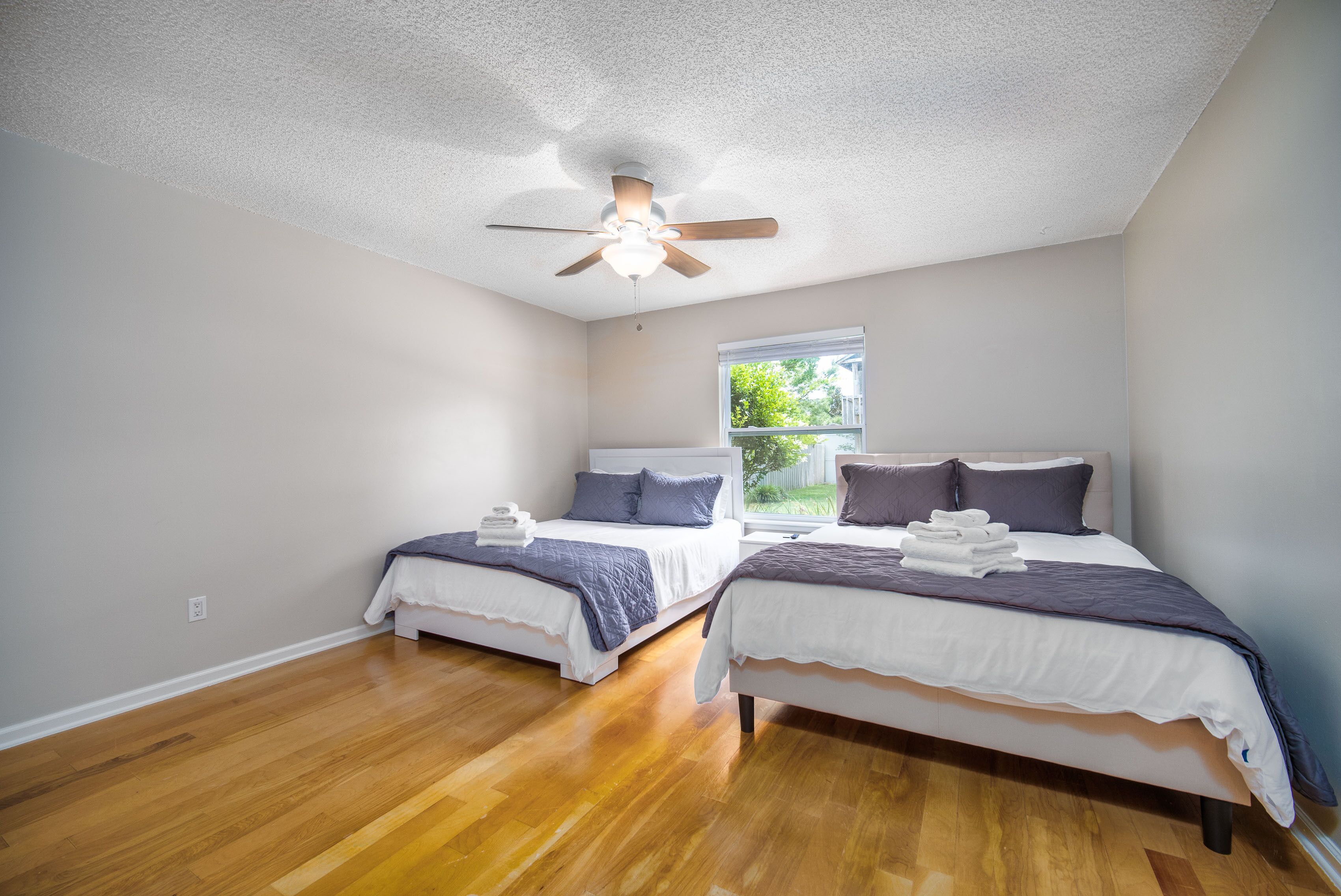A bedroom with two beds, a ceiling fan, and a window with a view of greenery.