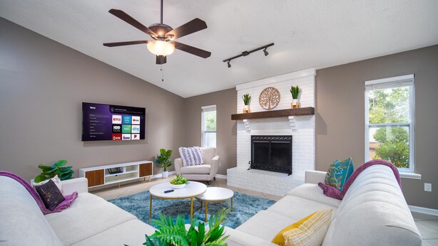 A modern living room with a fireplace, ceiling fan, and a flat-screen TV mounted on the wall.