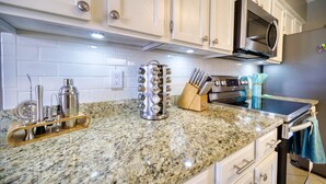 A kitchen with white cabinets, a stainless steel range hood, a microwave, and a granite countertop.
