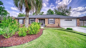 A two-story house with a brick exterior, a garage, and a well-maintained lawn with a palm tree.