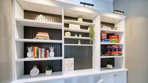 A white shelving unit with books, a clock, and decorative items.
