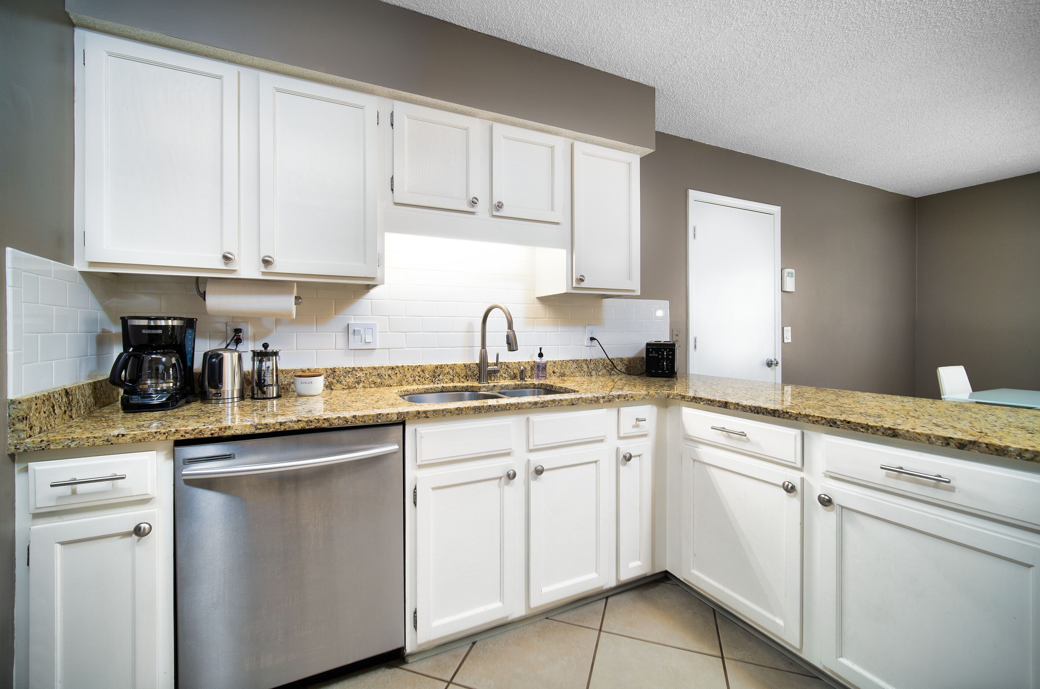 A kitchen with white cabinets, a granite countertop, stainless steel appliances, and a built-in dishwasher.
