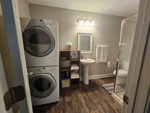 Une petite salle de bain Ă©quipĂ©e dâun lave-linge, dâun lavabo, dâun miroir et dâune douche.
