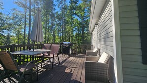 A wooden deck with outdoor furniture, a grill, and a view of tall trees.