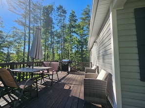 En træterrasse med udendørs møbler, grill og udsigt til høje træer.