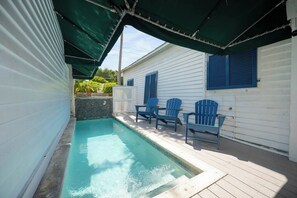 A swimming pool with a wooden deck, blue chairs, and a covered area with a green canopy.