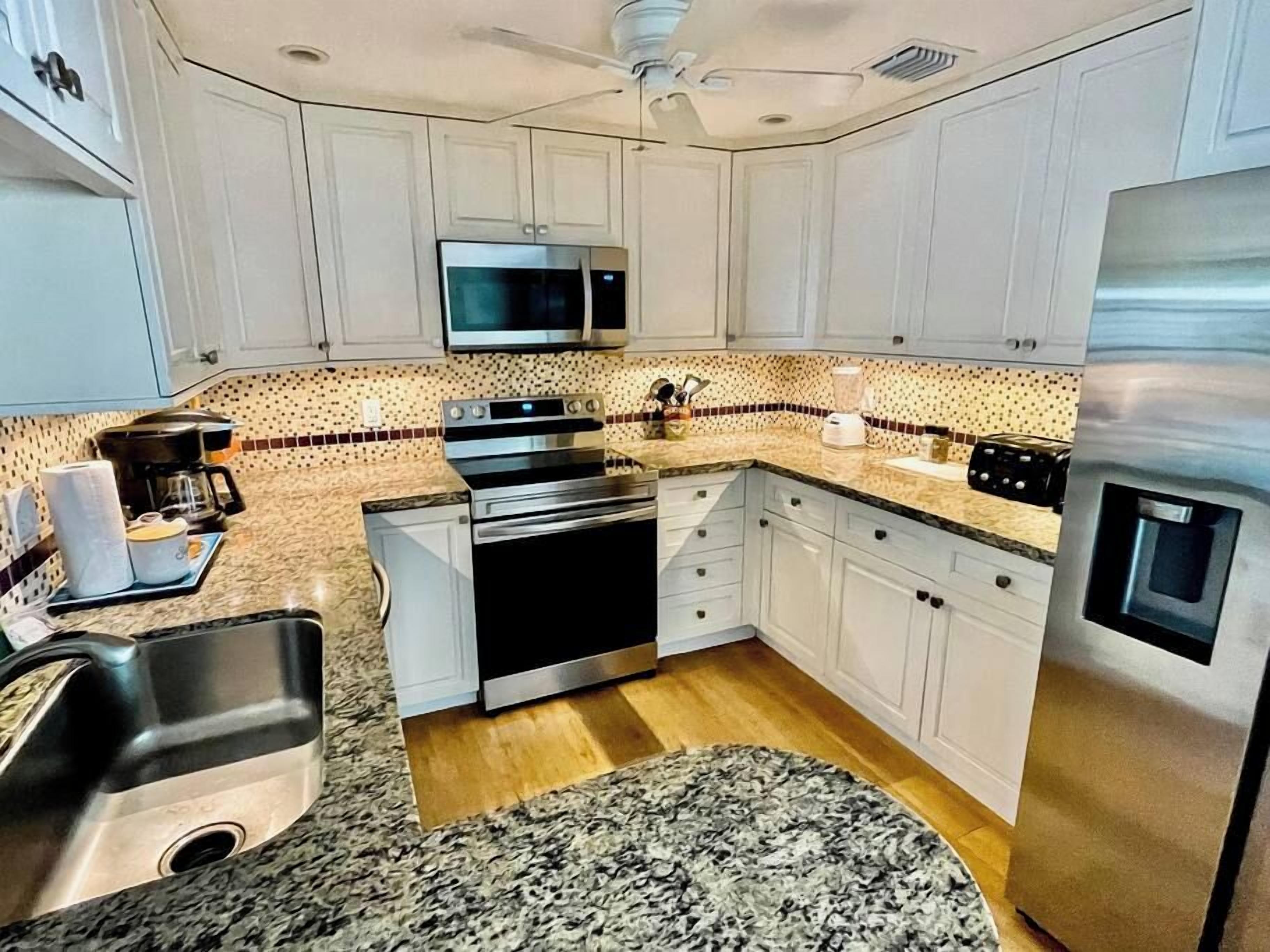 A kitchen with white cabinets, stainless steel appliances, a granite countertop, and a patterned backsplash.