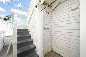 Eine Treppe führt zu einer weißen Außentür, mit einem weißen Zaun und einem Gebäude im Hintergrund.