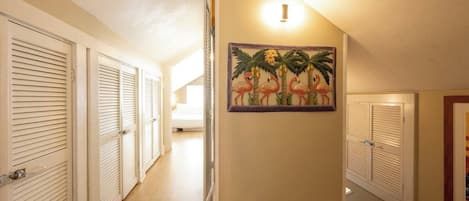 A hallway with closed louvered doors, a wall-mounted light fixture, and a framed tropical-themed artwork.