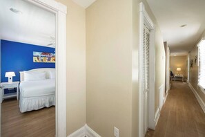 A hotel corridor with a bed in the adjacent room, a nightstand, and a lamp.